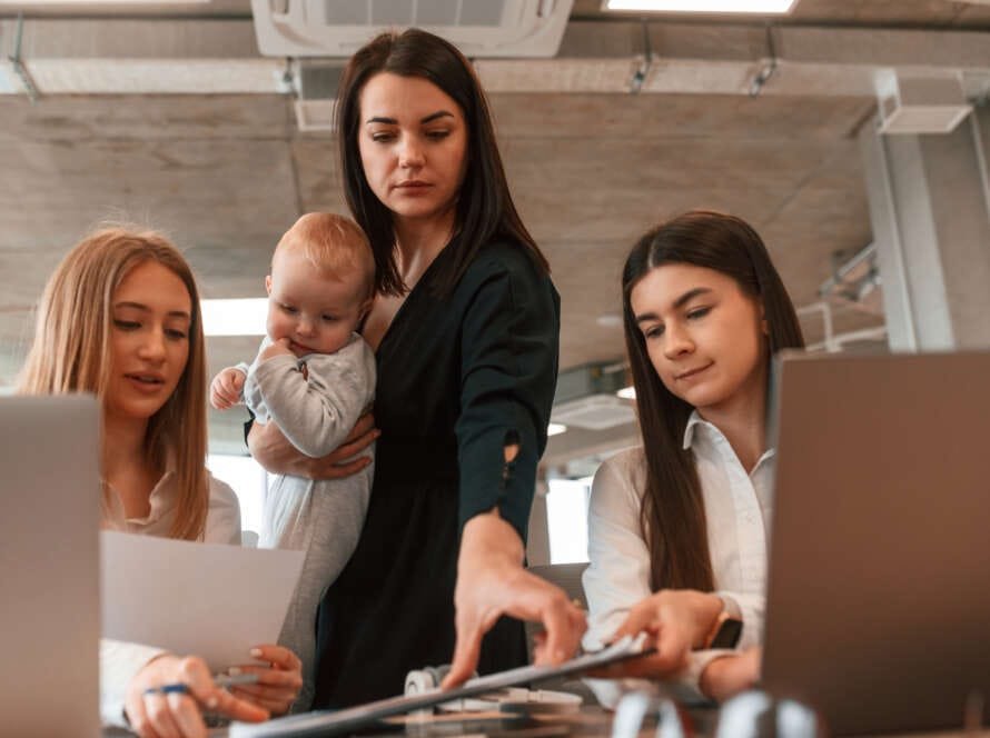 Mujer trabajadora con su bebé en una oficina, reflejando los desafíos de la maternidad y la brecha salarial de género en el entorno laboral.